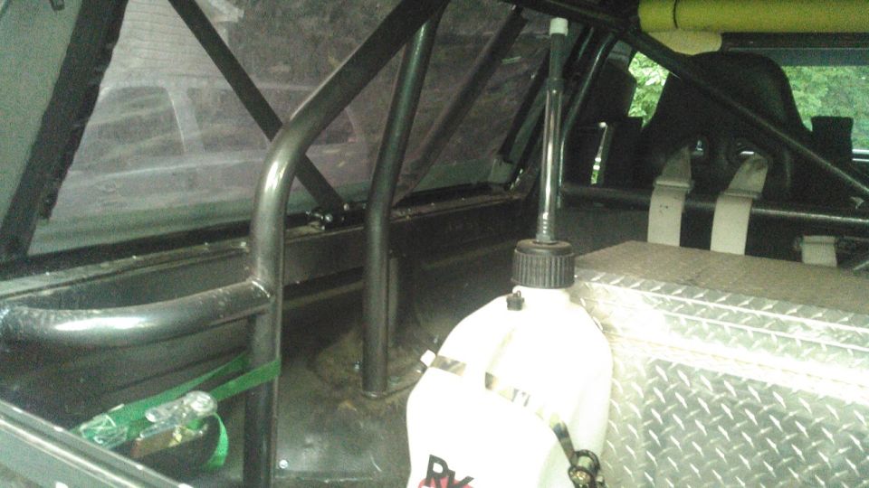 Interior of a modified vehicle with roll cage, racing seat, fuel jug, and toolbox.