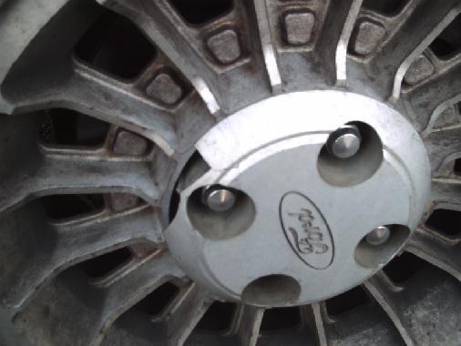 Close-up of multi-spoke aluminum wheel with Ford-oval center cap and exposed lug nuts