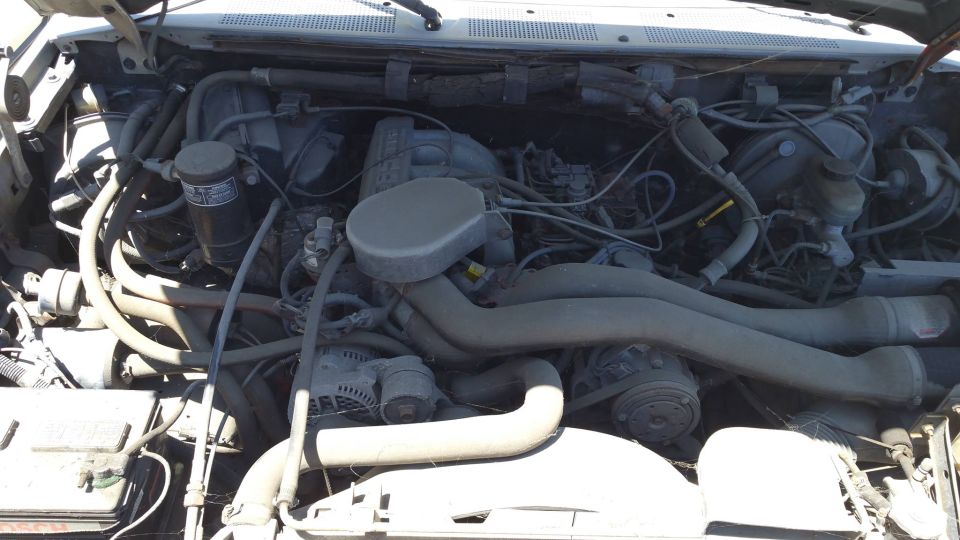 Engine bay of a 1990 Ford Bronco with dusty engine components and hoses.