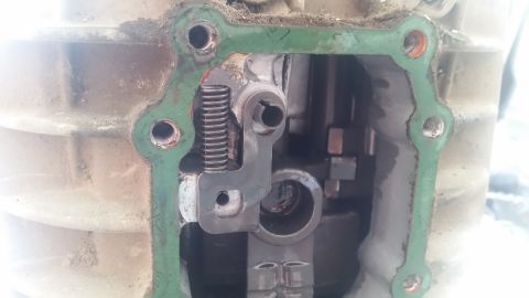1985 Ford Bronco - A close-up view of the internal components of a transmission, showing a shift fork mechanism with a spring and pivot points. The green gask…