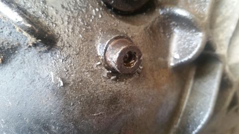 1985 Ford Bronco - A close-up shot shows a bolt with a hex socket head, likely a drain plug, on a greasy, metallic surface. The bolt appears to be slightly da…