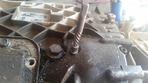 1985 Ford Bronco - A close-up view shows a screw extractor tool inserted into a threaded hole on a dirty, cast-iron automotive component, likely a transmissio…