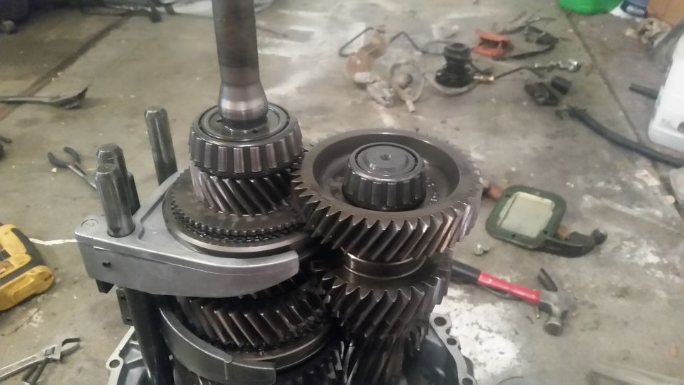 Disassembled manual transmission gears and shafts on a concrete floor with tools.
