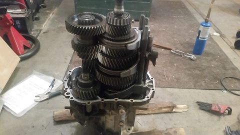 1985 Ford Bronco - A disassembled manual transmission is laid out on a concrete floor, with various gears and components visible within the transmission housi…