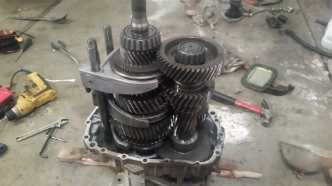 1985 Ford Bronco - A disassembled manual transmission is laid out on a concrete floor amidst various tools including a drill, wrenches, and a hammer. The tran…