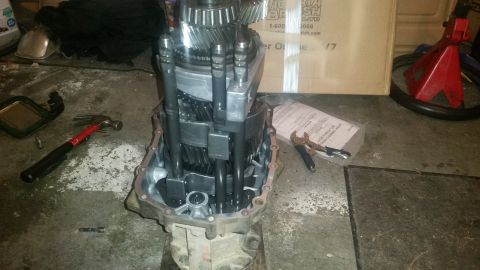 1985 Ford Bronco - A disassembled manual transmission is laid out on a concrete floor, surrounded by tools and a cardboard box. The transmission's internal ge…