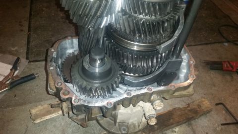 1985 Ford Bronco - A close-up view shows the internal gears of a manual transmission, partially disassembled and resting on wooden blocks. Tools, including a…