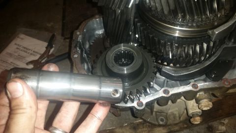 1985 Ford Bronco - A hand holds a metal shaft in front of a disassembled transmission with visible gears and housing. A manual for an Intex inflatable boat is…