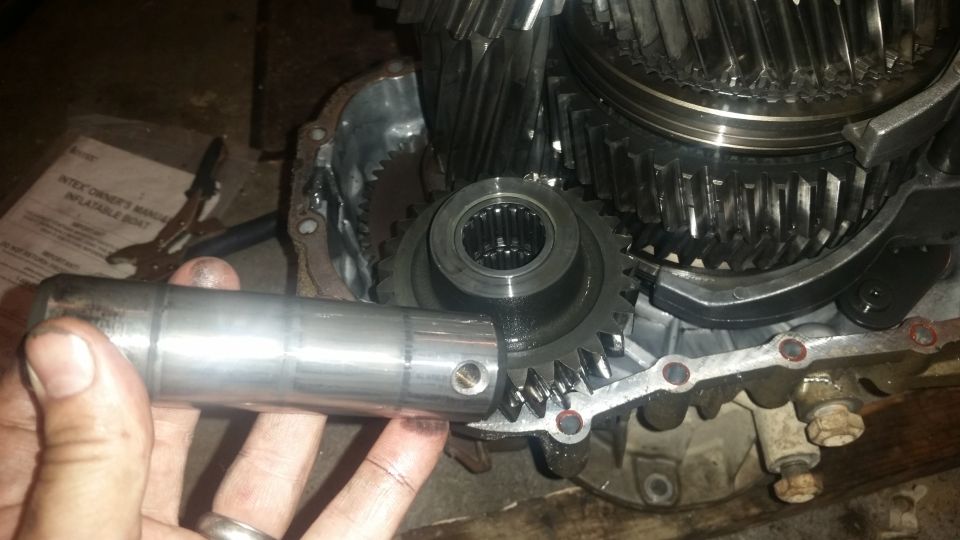 Hand holding metal shaft in front of transmission gears