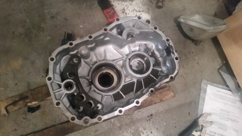 1985 Ford Bronco - A disassembled aluminum transmission case sits on a concrete floor, resting on wooden planks. The interior of the case shows signs of wear…