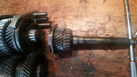 1985 Ford Bronco - A close-up view shows a disassembled transmission with gears and shafts laid out on a wooden surface. The parts appear to be from a manual…