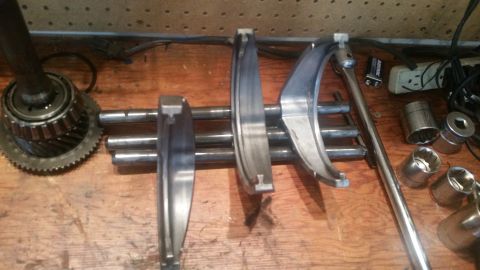 1985 Ford Bronco - A collection of metal parts, including gears, bearings, and what appear to be transmission components, are laid out on a wooden surface nex…