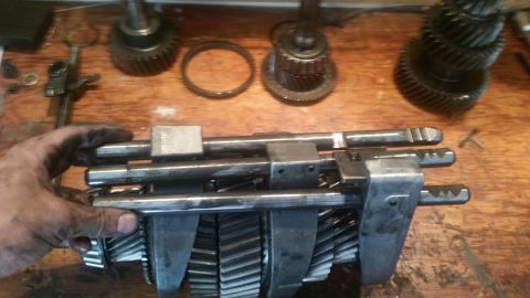 1985 Ford Bronco - A close-up shot shows a mechanic's dirty hands holding a transmission input shaft with gears. Several other gears and transmission componen…