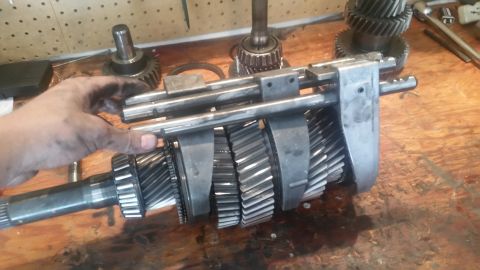 1985 Ford Bronco - A person's greasy hand is shown holding a disassembled manual transmission gear set. The gears are made of metal and are arranged on a shaf…