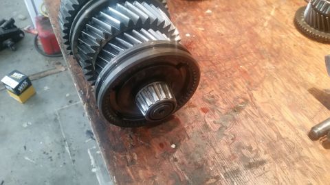 1985 Ford Bronco - A close-up view of a transmission input shaft and gears resting on a wooden workbench. A small box with "WIX" branding is visible in the ba…