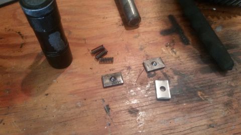 1985 Ford Bronco - Several small metal parts and springs are scattered on a wooden surface. A black cylindrical object is visible on the left side of the imag…