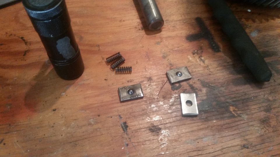 Metal parts and springs on a wooden surface with a black cylinder.