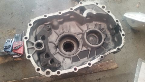 1985 Ford Bronco - A disassembled aluminum transmission casing is shown from a top-down perspective, resting on a wooden plank. Several sets of hex wrenches a…