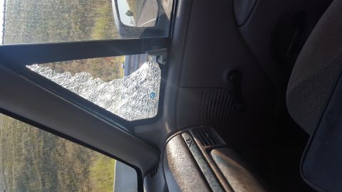 1995 Ford Bronco - The interior of a vehicle shows a cracked driver's side window with a view of the road and trees outside. The dashboard and seat are visibl…