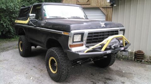 1978 Ford Bronco - A lifted, black 1978 Ford Bronco with yellow accents sits parked on a gravel surface in front of a wooden structure. The vehicle features l…