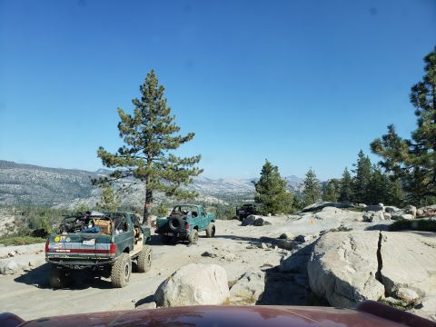 1968 Ford Bronco - Two off-road vehicles are parked on a rocky terrain with a mountainous landscape in the background under a clear blue sky. The vehicle in t…
