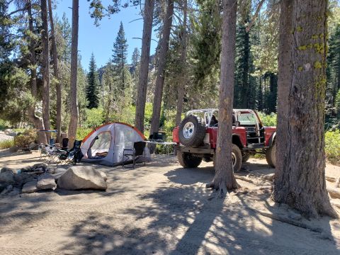 1968 Ford Bronco - A red Ford Bronco with a white roll cage is parked at a campsite next to a tent and camping chairs.