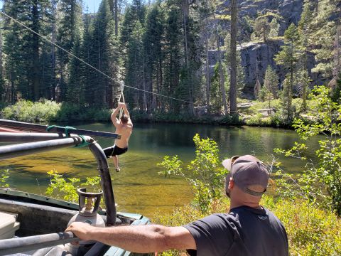 1968 Ford Bronco - A person is ziplining over a clear lake, with a vehicle in the foreground that appears to be a 1968 Ford Bronco.