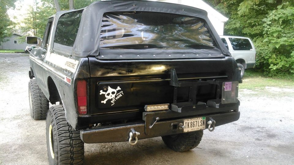 Black lifted Ford Bronco with soft top, custom rear bumper, and skull sticker.