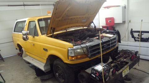 1996 Ford Bronco - A yellow Ford Bronco with its hood open is parked in a garage, with the engine exposed and various tools and parts around it. The vehicle a…