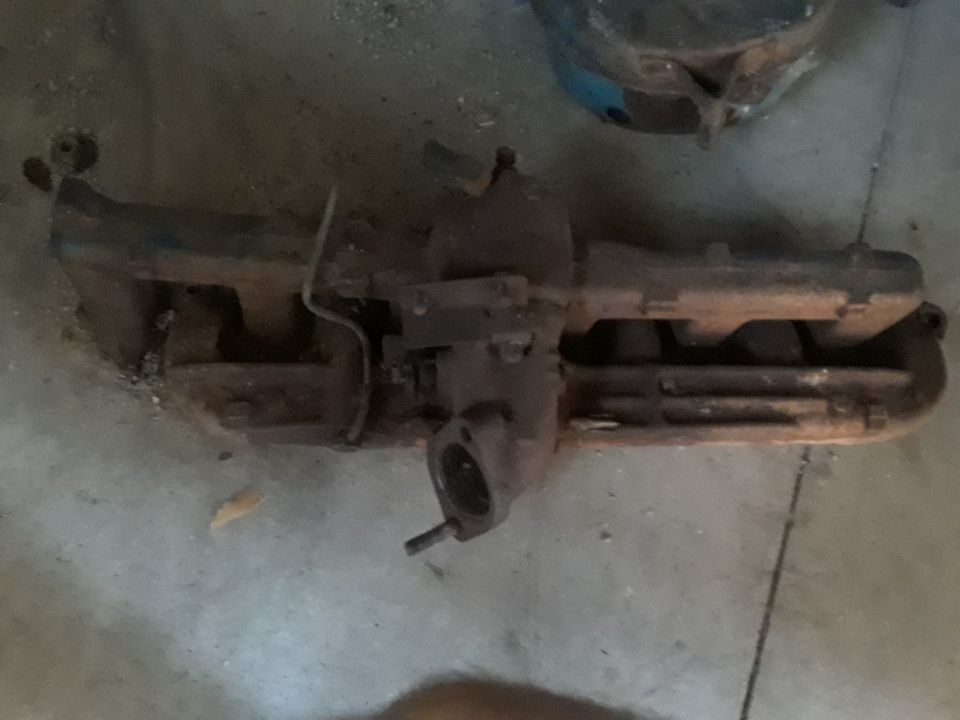 Rusty exhaust manifold with carburetor on concrete floor