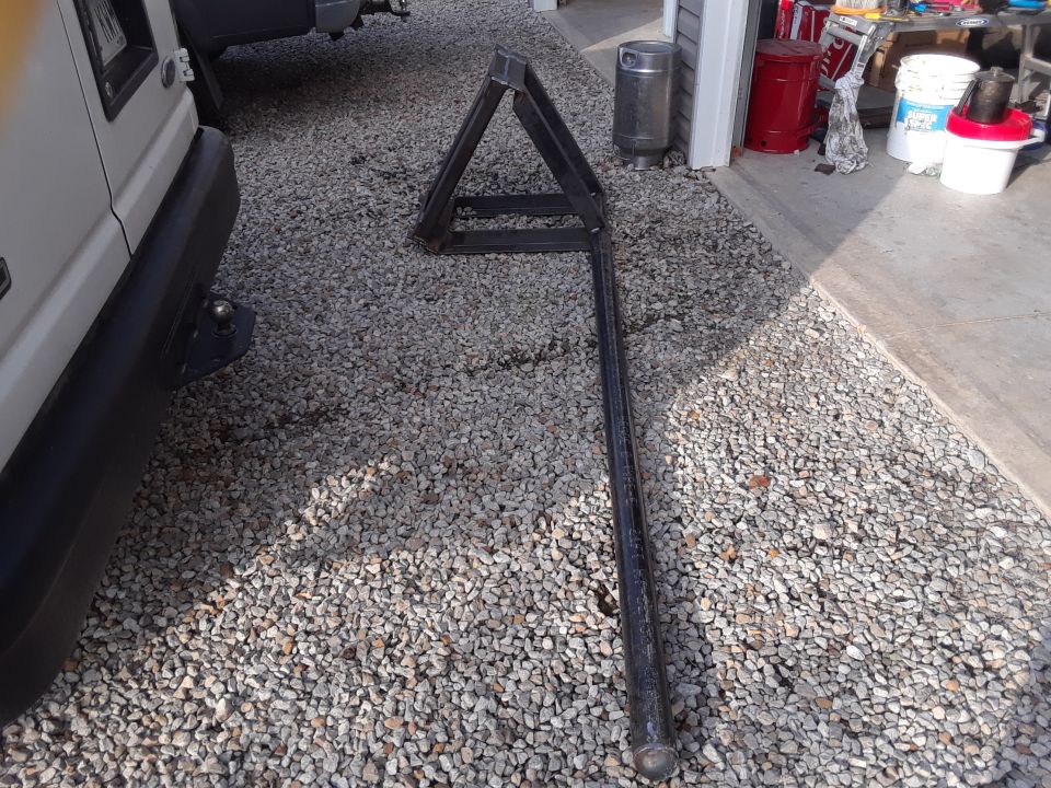 Custom metal attachment with triangular frame on gravel next to a white vehicle.