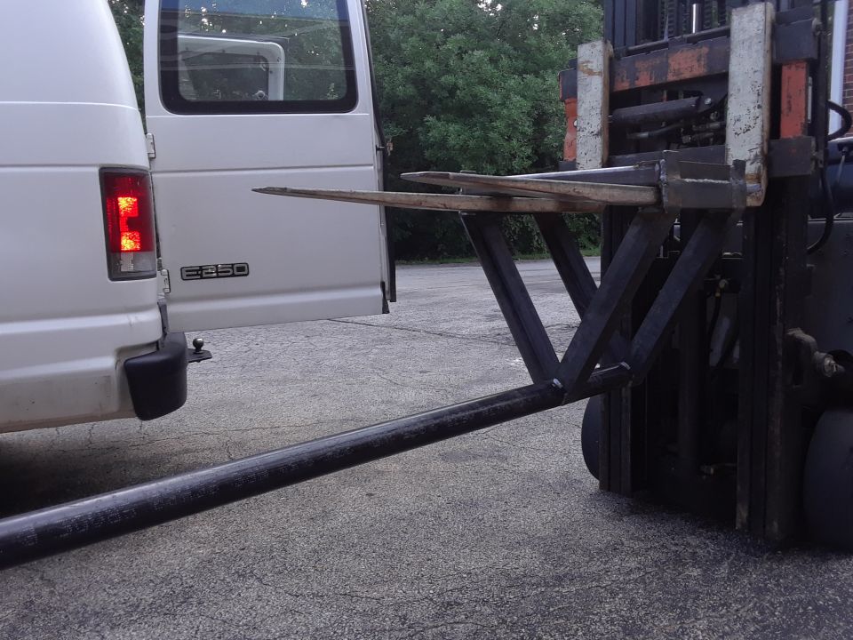 White Ford E-Series van with rear door open, next to a forklift with extended forks.