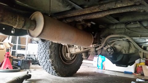 1985 Ford Bronco - Underside view of a vehicle, showing the exhaust system, rear differential, and a large tire. The vehicle appears to be on jack stands in a…