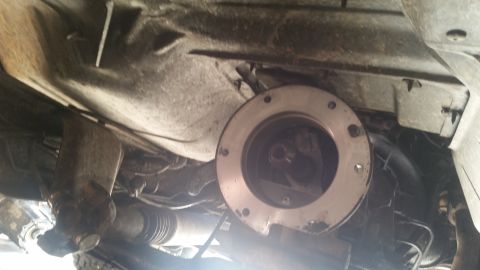 1985 Ford Bronco - The underside of a vehicle shows a transfer case or transmission adapter plate. A driveshaft and part of the exhaust system are also visibl…