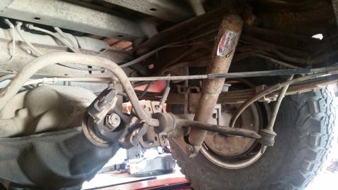 1985 Ford Bronco - Underside view of the rear suspension of a vehicle, showing the differential, leaf springs, shock absorber, and sway bar components.