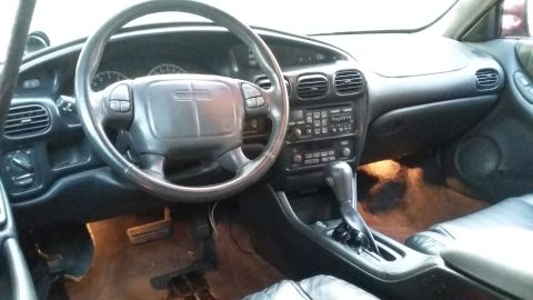 2000 Pontiac Grand Prix - The interior of a car is shown, featuring a steering wheel, dashboard with radio and climate controls, and a center console with a gear shi…