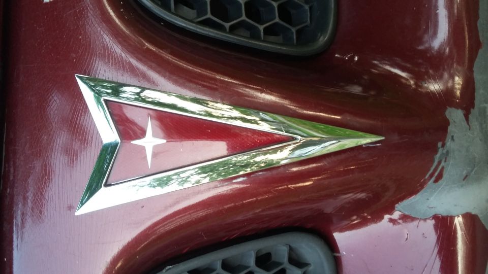 Close-up of a red Pontiac emblem on a scratched dark red car.