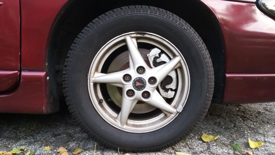 Maroon Pontiac Grand Prix front wheel and tire with silver five-spoke alloy wheel and Cooper Cobra tire.
