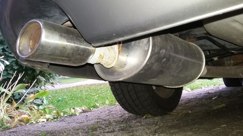 Dual stainless-steel exhaust mufflers mounted under a vehicle, viewed from below near a rear tire