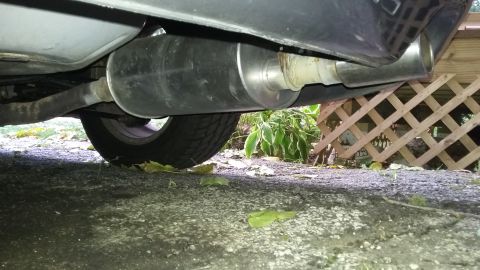 Underneath a car showing the exhaust pipe, muffler, and rear tire.