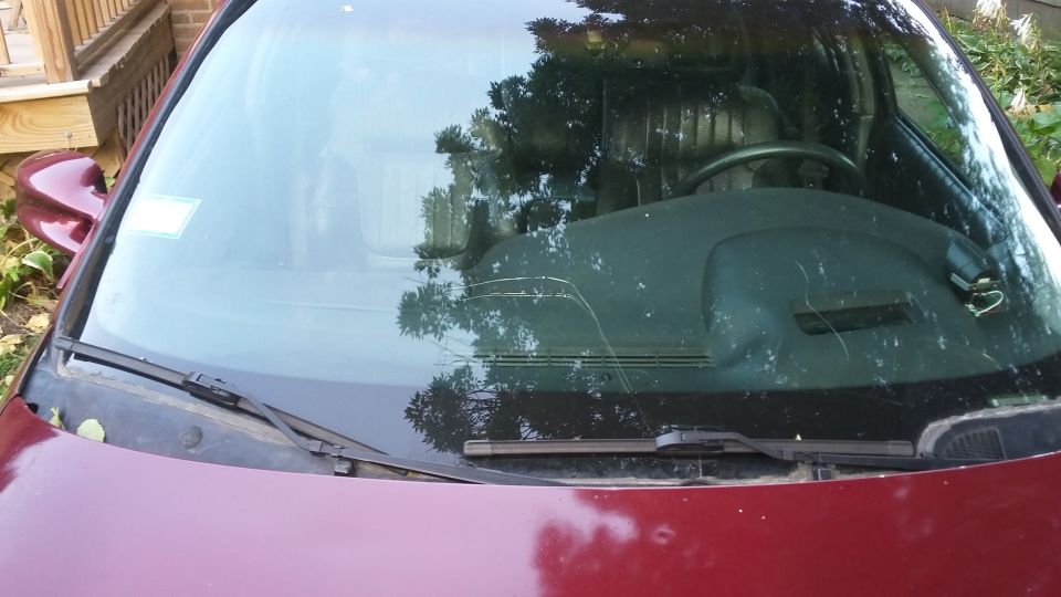 Front windshield of a dark red car with a crack and interior reflections.