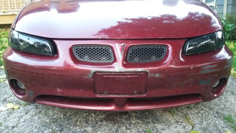 Dark red Pontiac Grand Prix front end with smoked headlights and worn bumper.