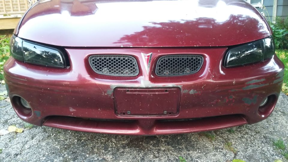 Dark red Pontiac Grand Prix front end with smoked headlights and worn bumper.