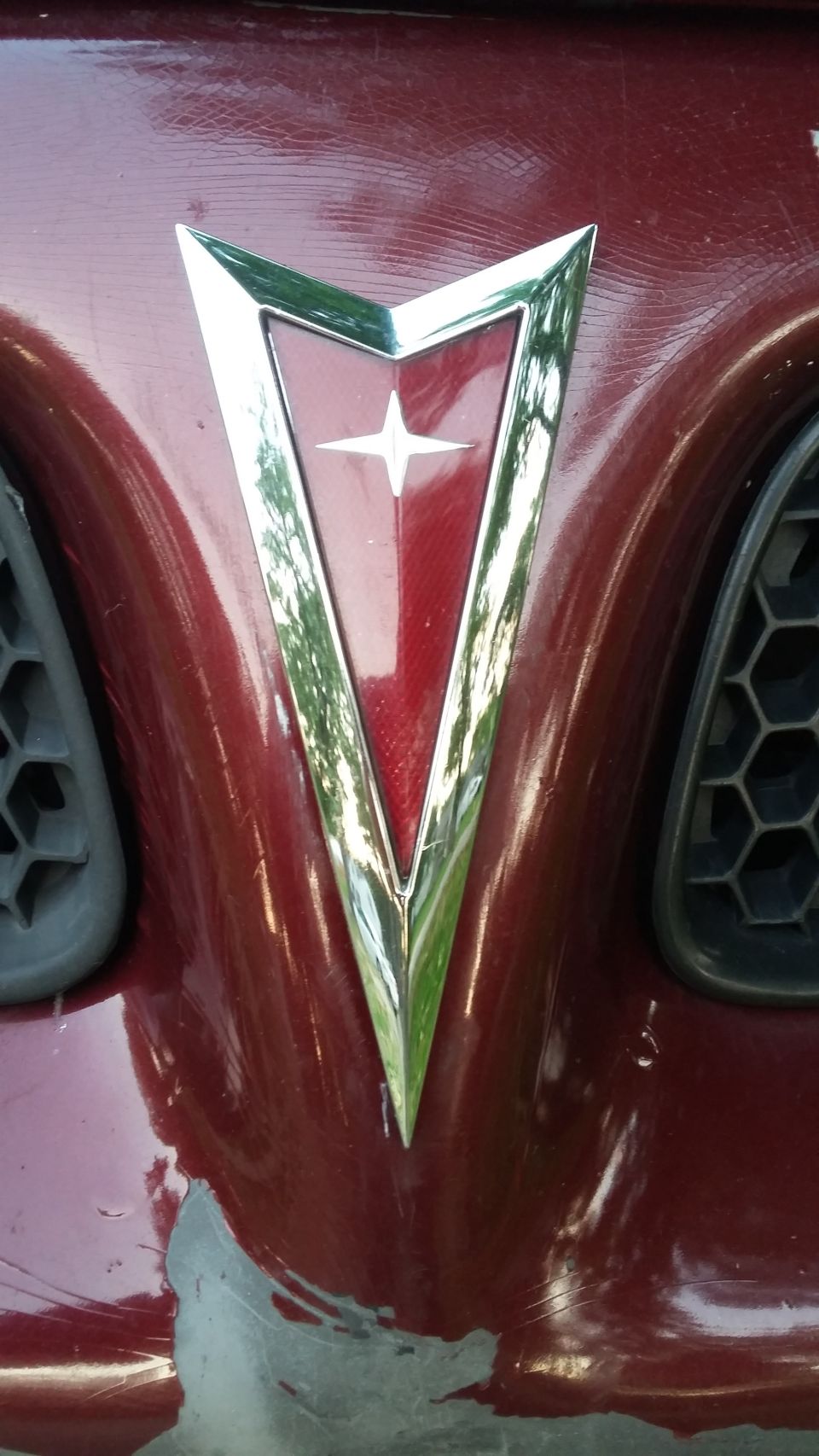 Pontiac emblem on a dark red car with visible paint damage.