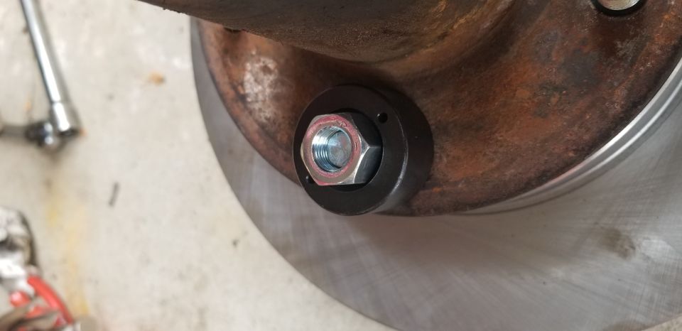 Close-up of lug nut being tightened on a rusty brake rotor with a socket tool.