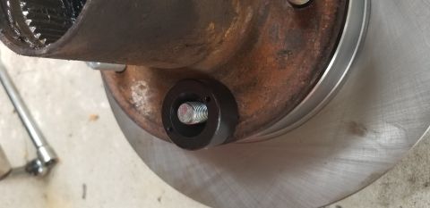 1995 Ford Bronco - A close-up view shows a metal hub with splines, attached to a rusty brake rotor. A black circular tool with a threaded bolt is mounted to t…