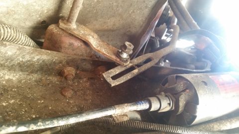 1985 Ford Bronco - This is a close-up view of rusty mechanical linkage and a starter motor, likely from the undercarriage of a vehicle. A cable runs across th…