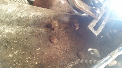 1985 Ford Bronco - This image shows a close-up view of heavily rusted metal components and bolts, likely from a vehicle's chassis.
