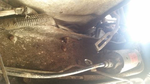 1985 Ford Bronco - Close-up view of the starter motor and associated wiring on the underside of a vehicle, likely part of an engine or drivetrain component.