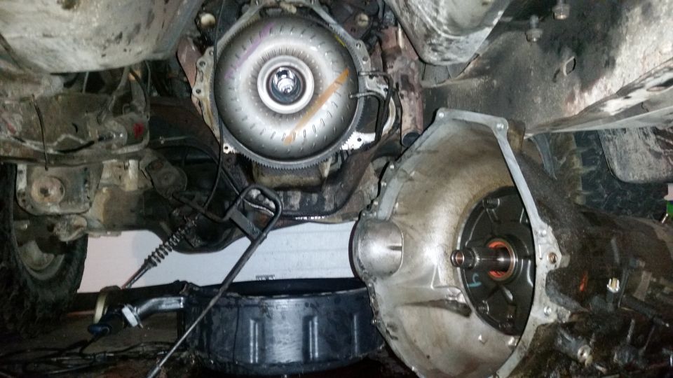 Underside view of a disassembled vehicle transmission and torque converter with a drain pan
